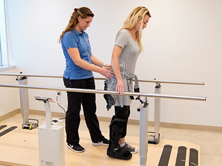 Orthopedic patient with a leg injury walks with therapist's help.
