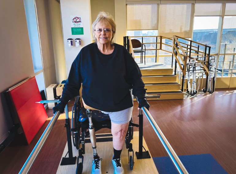 Patsy smiling at the camera while she works on the parallel bars.