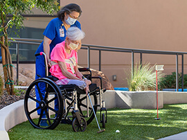 Woman in wheelchair with amputated legs plays mini golf with therapist.