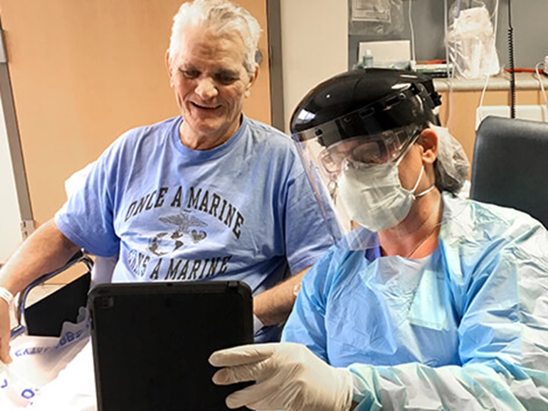 Therapist in protective equipment talks to patient.
