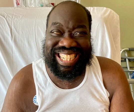 Derrick Holt smiling ear-to-ear for a picture in his hospital bed.