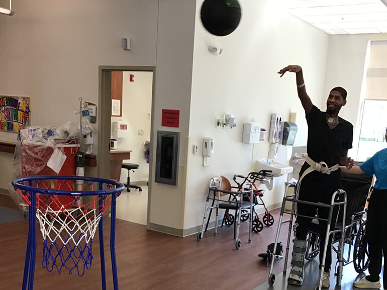Ryan Carter shoots a basketball into a basketball hoop in a therapy center.