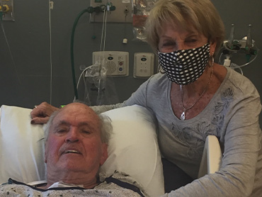 Bill Young lying in hospital bed with his wife beside him.
