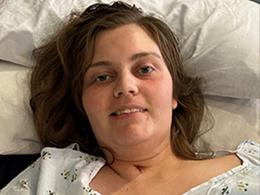 Stacy Chavez smiling for a picture while lying down in her hospital bed. 