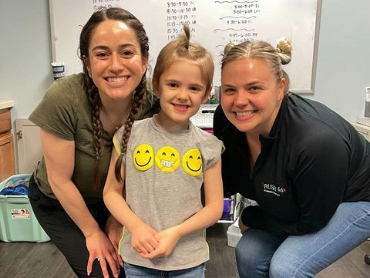 Reid Johnson smiling for a picture with her two pediatric physical therapists.