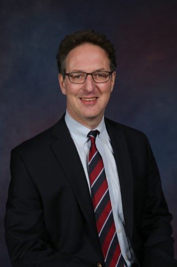 Bruce Pomeranz smiles at the camera for a headshot wearing a black suit jacket and striped tie.