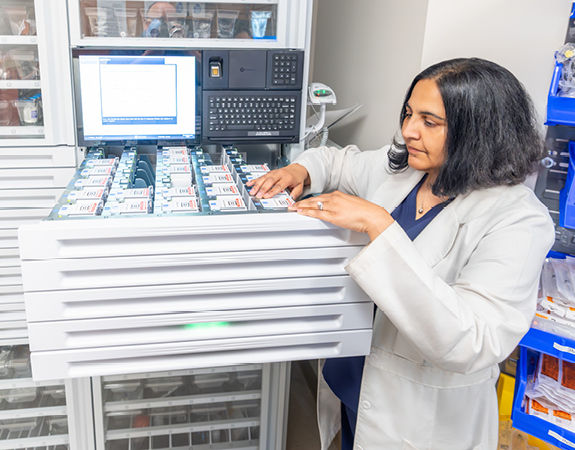 A pharmacist accesses medicine for a patient from a secured drawer.