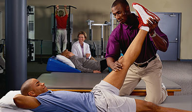 Patient lays on his back on a table while physical therapist stretches his leg.