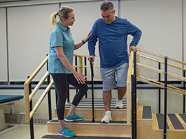 Therapist assisting patient as they walk down stairs with a cane