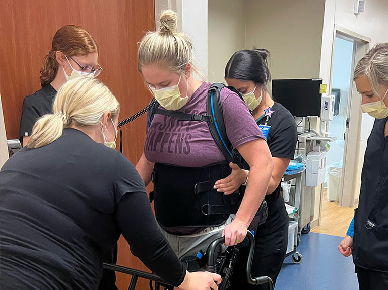 Alisha Tomac balancing with her walker and therapy equipment with assistance from her personal care team. 