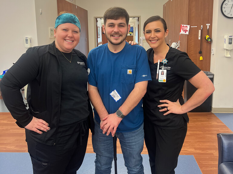 Drew stands in a hospital hallway with two of his therapists.