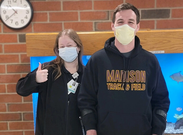 John standing with his prosthetics next to his therapist wearing a mask.