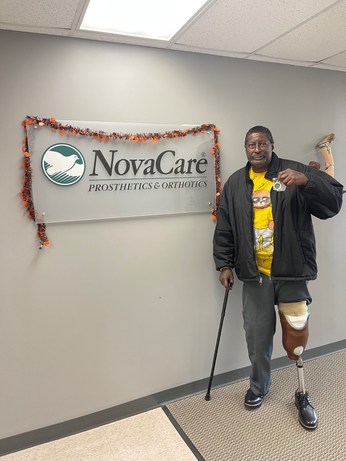 A patient named Robert posing in front of the NovaCare logo with his prosthetic.