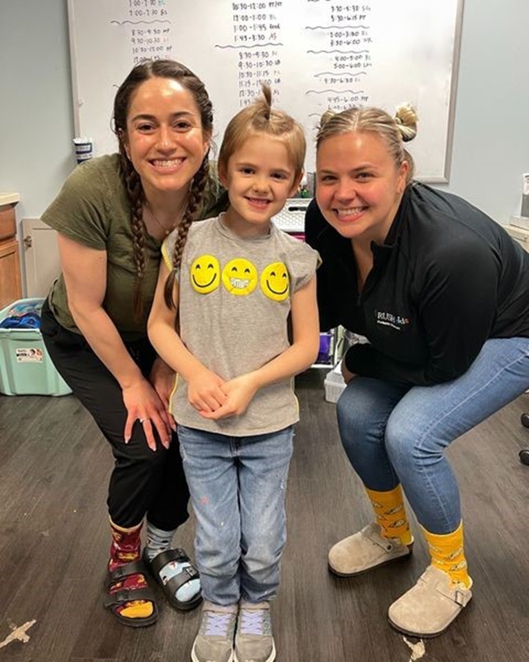 Pediatric therapy patient, Reid, stands with her care team smiling.