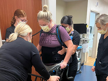 Alisha Tomac balancing with her walker and therapy equipment with assistance from her personal care team. 
