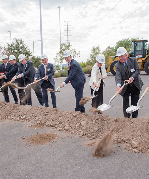 Group of men in suits work together to dig with shovels during a groundbreaking ceremony.