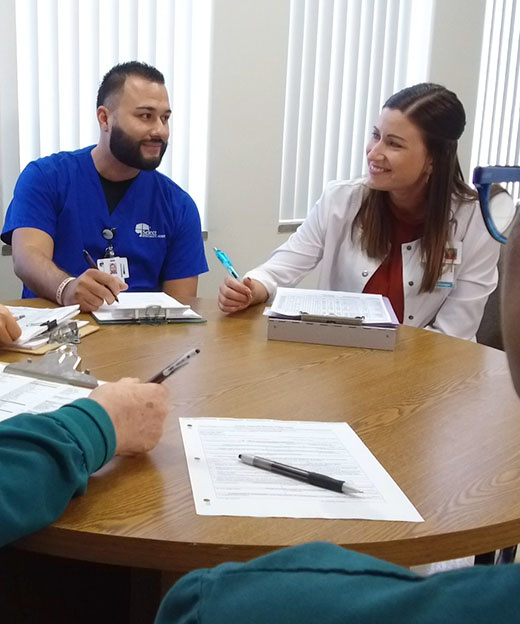 Patient care team sit at a table and discuss patient care while smiling.