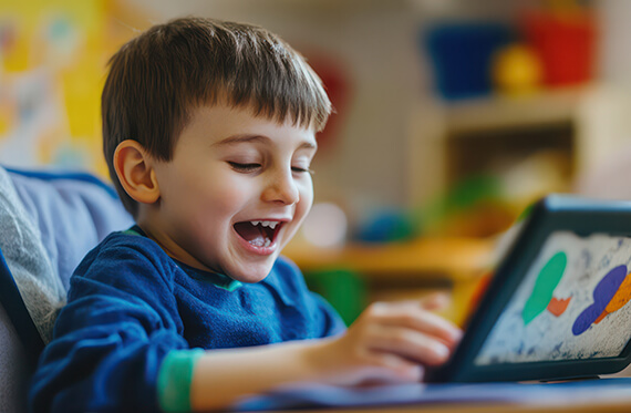 A child smiling as he uses his tablet in a classroom