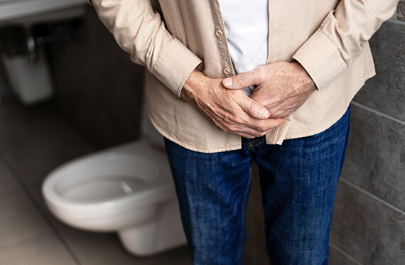 Close up of a man holding his lower stomach and a toilet in the background