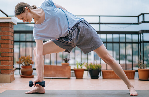 Woman lunging to the side with small dumbbell on a yoga mat. 