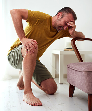 Man kneeling on ground with painful expression while leaning on chair.