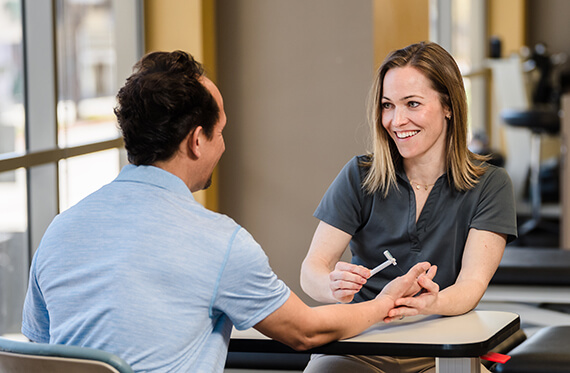 A hand therapist is sitting across from a patient and using IASTM on a patient's hand