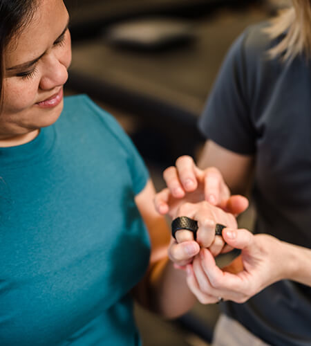 A close up of a patient practicing hand manipulation while a therapist assists her fingers