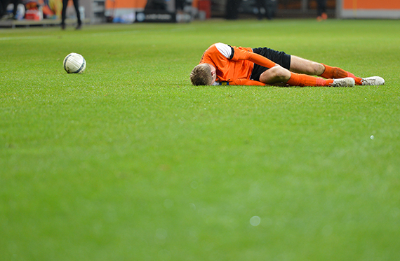 A soccer player is laying on the soccer field in pain and a soccer ball is sitting nearby