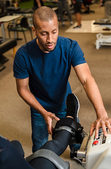 A patient's knee is in a machine while a physical therapist is examining the knee