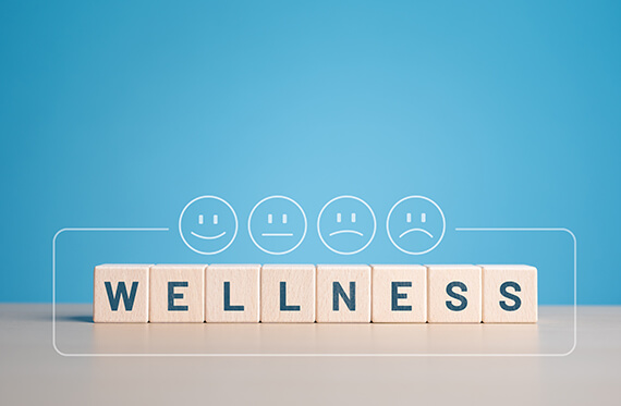 Block on a table that spell out "wellness" with various happy and sad face icons above
