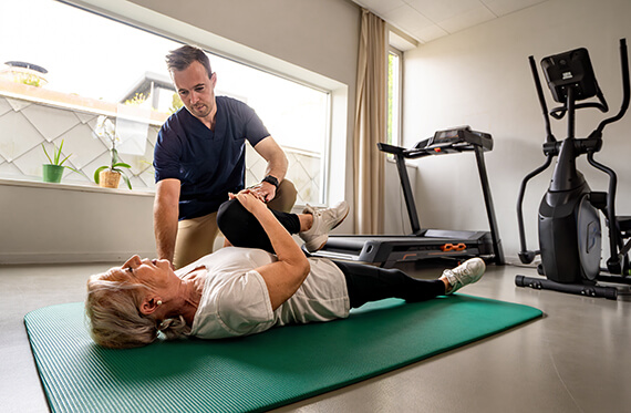 Patient laying on her back on the floor while a therapist helps her bring one knee to her chest