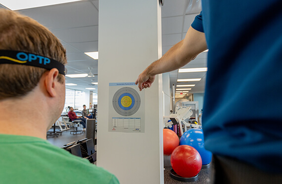 A boy is looking at a poster on the wall to complete a visual concussion test while his therapist is pointing to the poster