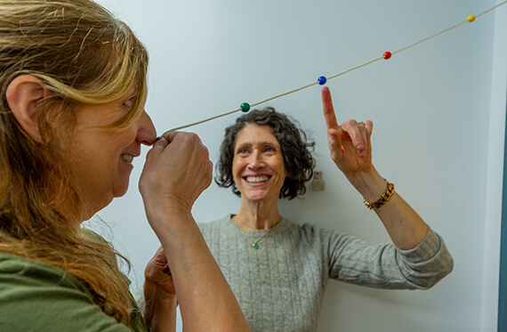 A close up of a woman completing a visual concussion test as her therapist is standing and smiling beside her