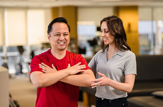 Cancer survivor is executing an upper body exercise while a cancer rehabilitation therapist is standing beside them