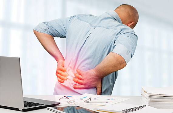 Man facing away from the camera holding his lower back in pain. There is redness on the lower back to highlight the pain