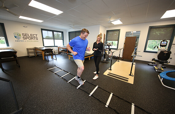 Athlete is completing an agility ladder drill while physical therapist is standing beside and observing