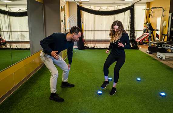 Athlete is about to step on a BlazePod for reaction training drill while a physical therapist is encouraging them
