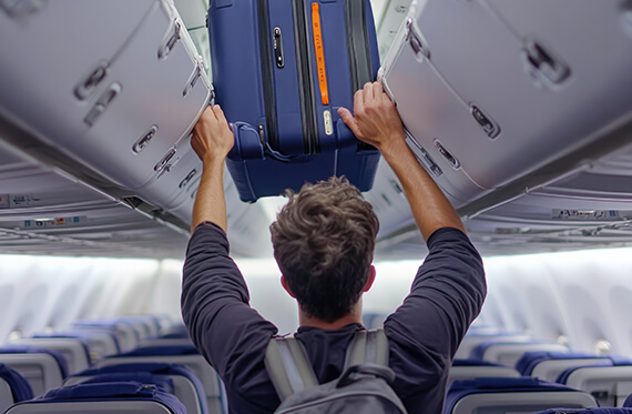 Man facing away from camera and placing his luggage in the overhead bin on a plane