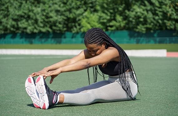 Girl in sportswear sitting on the ground outside and touching her toes
